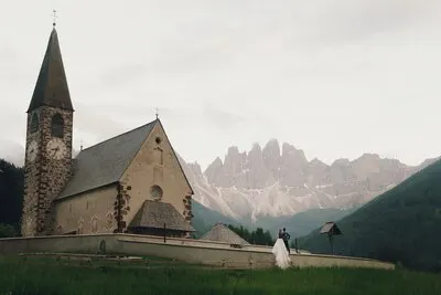 Kissing wedding couple stands before stone church in mountains