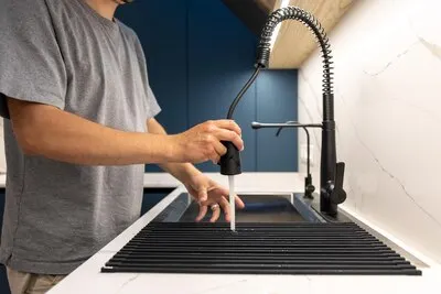 Man cleaning kitchen rack with pull out faucet sprayer rinsing the drainer