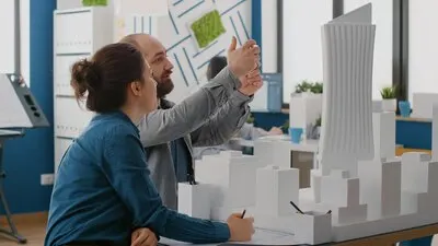 Architects using smartphone to design construction layout with building model and blueprints. Man and woman working with mobile phone to plan architectural structure and development.