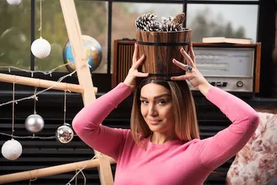 Beautiful woman holding bucket of pinecones on her head.