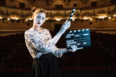 Smiling female mime artist holding clapperboard on stage