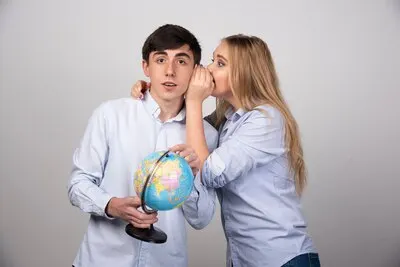 Excited young couple planning their holiday holding up a globe and whispering.