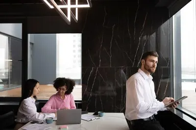 Man using a tablet to work while his female colleagues are using a laptop