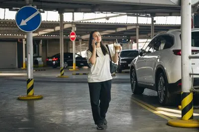 A young woman with coffee talking on the phone in the parking lot