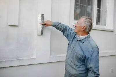 Old man standing near building with a repair tools