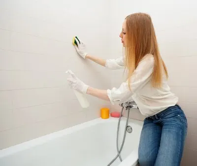 long-haired woman cleaning tile with sponge in bathroom