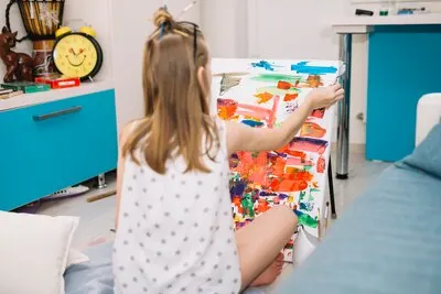 Girl in white sitting on floor and painting with gouache on canvas
