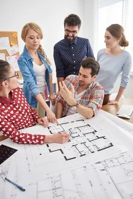 Coworkers at office with architecture plans and a computer