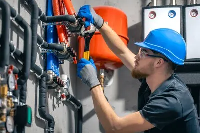 A man installs a heating system in a house and checks the pipes with a wrench