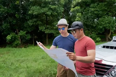 Asian male friends standing by car in rural road and looking at large map