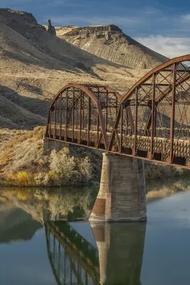 Vertical shot of a bridge over the river with mountains and a blue sky