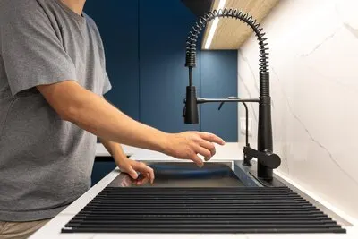 Person reaching for a matte black kitchen faucet before turning on water