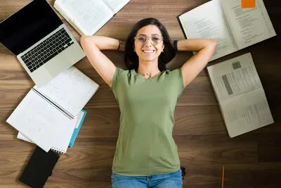 I finished my homework. Top view of a happy woman smiling and surrounded by books while resting after a productive study time for college