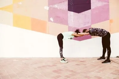 Man and woman stretching in front of graffiti wall