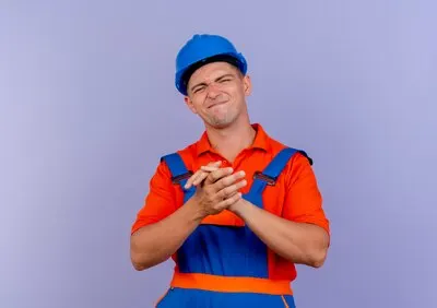 Pleased young male builder wearing uniform and safety helmet showing handshakes gesture on purple