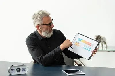 Older man at home showing graph on notepad with tablet on desk