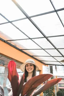 Close-up of red leaves in front of happy woman standing in greenhouse
