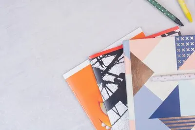 Set of notebooks on white surface with pen.