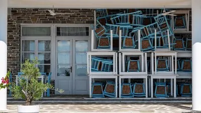 Terrace of a restaurant with assembled chairs and tables, small tree in front of the entrance in Nikiti, Greece