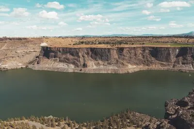 Landscape of a river surrounded by cliffs covered in greenery under a blue sky and sunlight