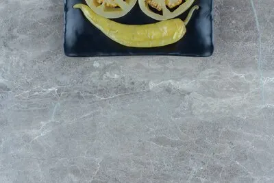 Top view of pickled hot pepper on black plate over grey background.