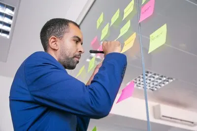 African American office employer writing on sticker with marker. Focused confident businessman in suit sharing idea for project and making note