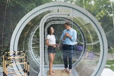 A couple entering inside transparent bubble tent at glamping Lush forest and nature around